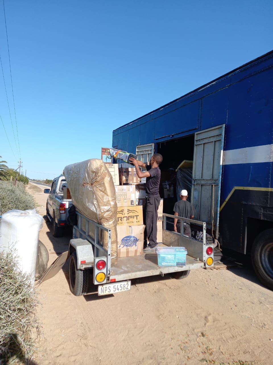 Workers loading packed boxes and wrapped items onto a trailer for long-distance transport